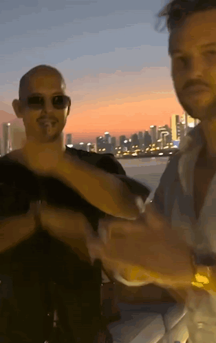 A Man Wearing Sunglasses Is Standing Next To Another Man GIF