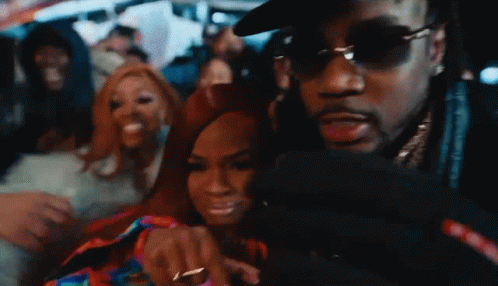 A Man Wearing Sunglasses Is Taking A Picture Of A Woman In A Crowd GIF