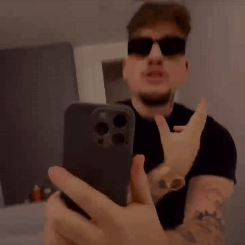 A Man Wearing Sunglasses Is Taking A Selfie With His Mouth Open While Holding A Cell Phone . GIF