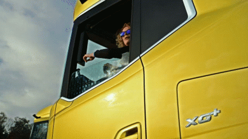 A Man Wearing Sunglasses Looks Out Of The Window Of A Yellow Truck GIF