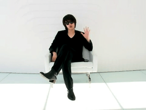 A Man Wearing Sunglasses Sits In A Chair With His Feet Crossed GIF