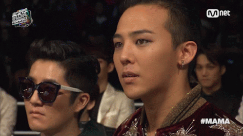 A Man Wearing Sunglasses Sits Next To A Man Wearing A Jacket With The Word Mama Written On It GIF