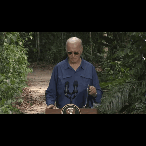 A Man Wearing Sunglasses Stands Behind A Podium With A United States Seal On It GIF