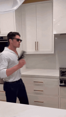 a man wearing sunglasses stands in a kitchen with white cabinets