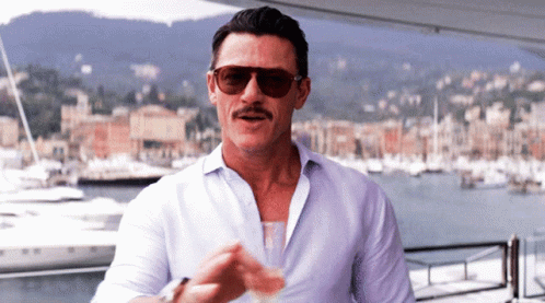 A Man Wearing Sunglasses Stands In Front Of A Marina GIF