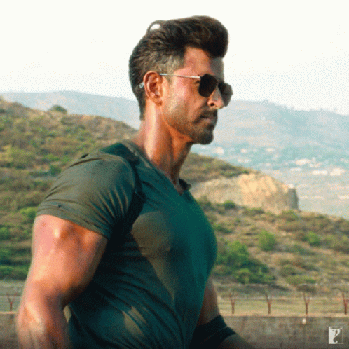 A Man Wearing Sunglasses Stands In Front Of A Mountain GIF