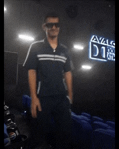 A Man Wearing Sunglasses Stands In Front Of A Sign That Says Avals GIF