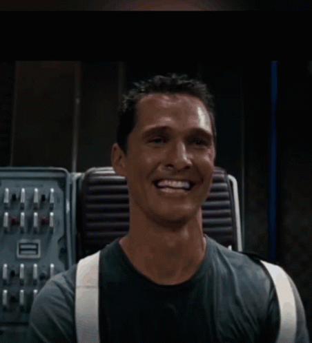A Man Wearing Suspenders Is Smiling In Front Of A Machine GIF