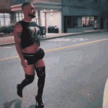 A Man Wearing Thigh High Boots And Shorts Is Walking Down A Street GIF