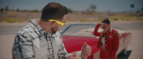 A Man Wearing Yellow Sunglasses Stands Next To A Woman In A Red Dress GIF