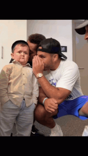 A Man Whispering Into Another Man 'S Ear While Holding A Small Boy GIF