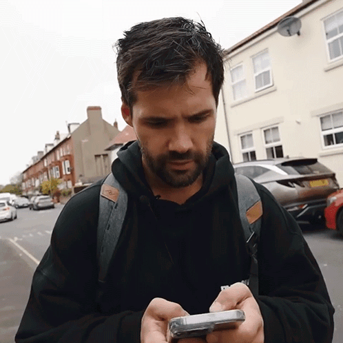 A Man With A Backpack Is Looking At His Cellphone GIF