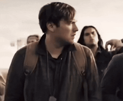 A Man With A Backpack Is Standing In A Crowd Of People And Looking At The Camera . GIF