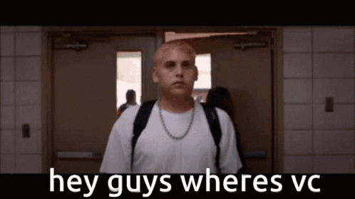 A Man With A Backpack Is Standing In A Hallway With The Words Hey Guys Wheres Vc Written Above Him . GIF