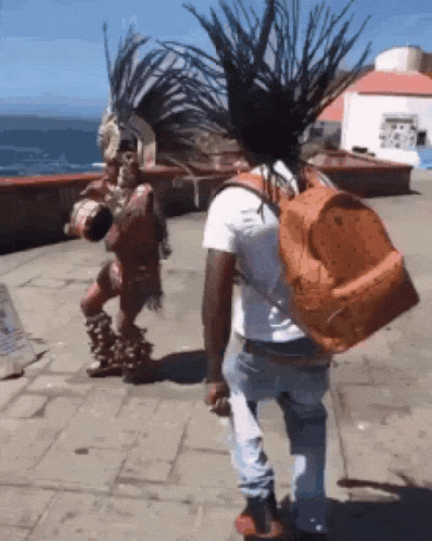 A Man With A Backpack Is Walking In Front Of A Native American GIF