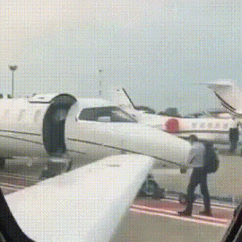 A Man With A Backpack Is Walking Towards A White Airplane . GIF