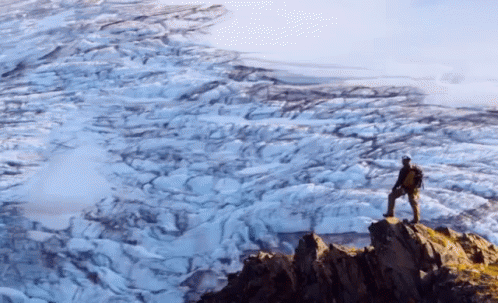 A Man With A Backpack Stands On Top Of A Snow Covered Mountain GIF
