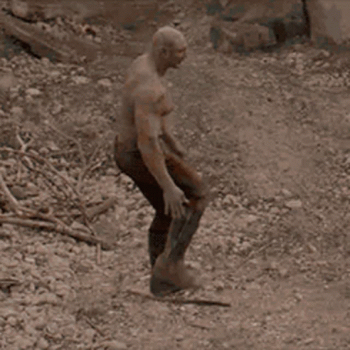 A Man With A Bald Head Is Standing In The Dirt Holding A Sword . GIF