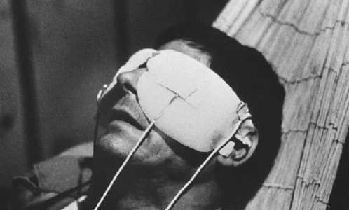 A Man With A Bandage On His Eye Is Laying On A Bed GIF