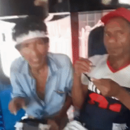 A Man With A Bandage On His Head Is Sitting Next To Another Man Wearing A Red Hat GIF