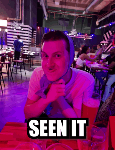 A Man With A Bandage On His Head Sits At A Table With A Sign That Says Seen It On It GIF