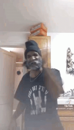 A Man With A Beard And A Beanie Is Standing In A Room . GIF