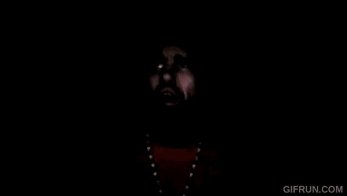 A Man With A Beard And A Beanie Is Wearing A Yellow Shirt And Necklace . GIF
