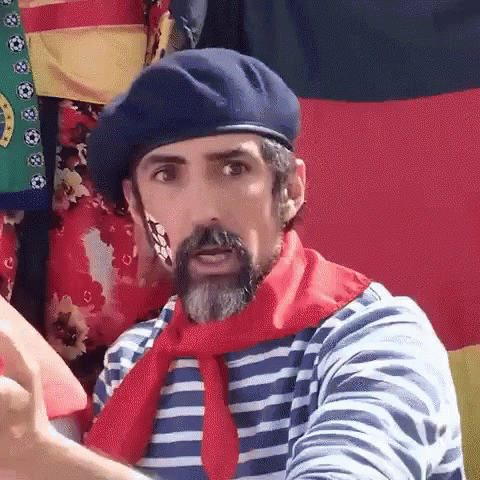 A Man With A Beard And A Beret Is Wearing A Striped Shirt And A Red Scarf . GIF
