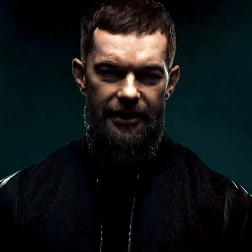 A Man With A Beard And A Black Jacket Is Looking At The Camera GIF
