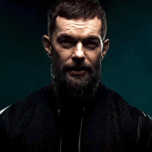 A Man With A Beard And A Black Jacket Is Looking At The Camera GIF