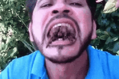 A Man With A Beard And A Blue Shirt Is Making A Funny Face . GIF