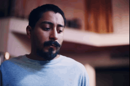 A Man With A Beard And A Blue Shirt Looks Down GIF
