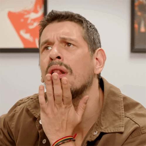 A Man With A Beard And A Brown Shirt Is Covering His Mouth With His Hands GIF