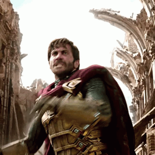 A Man With A Beard And A Cape Is Standing In Front Of A Ruined Building GIF