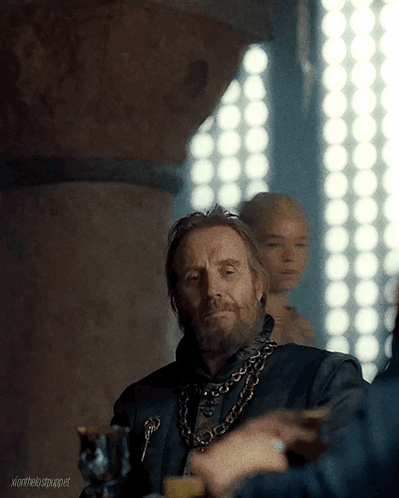 a man with a beard and a chain around his neck is sitting at a table with other people .
