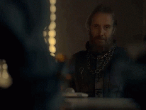 a man with a beard and a chain around his neck is sitting at a table with other people .