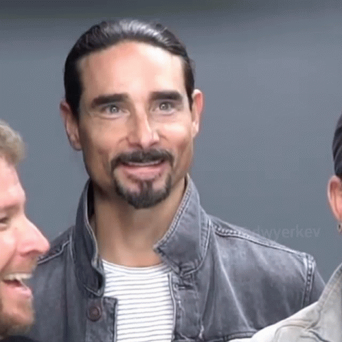 A Man With A Beard And A Denim Jacket Smiles GIF