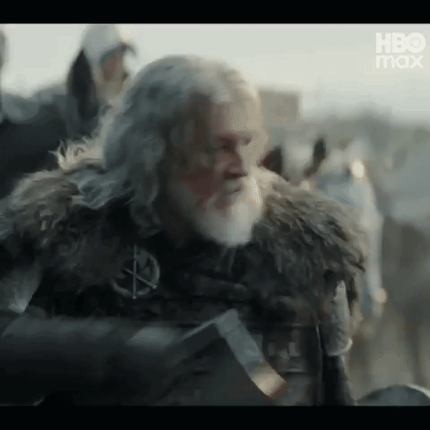 A Man With A Beard And A Fur Coat Is Holding A Sword In His Hand . GIF