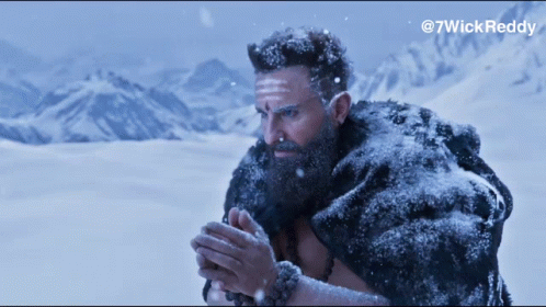 A Man With A Beard And A Fur Coat Is Standing In The Snow With Mountains In The Background GIF