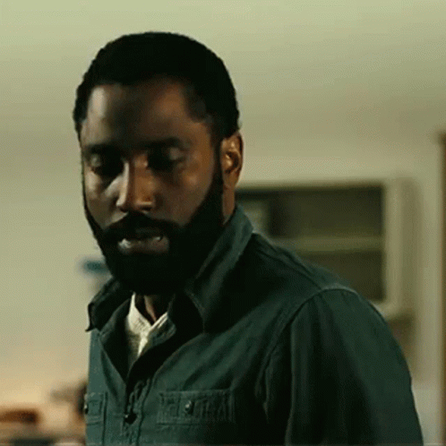 A Man With A Beard And A Green Shirt Is Standing In A Room . GIF