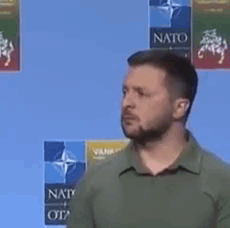 A Man With A Beard And A Green Shirt Is Standing In Front Of A Blue Background . GIF