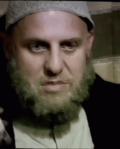 A Man With A Beard And A Hat Is Making A Face . GIF