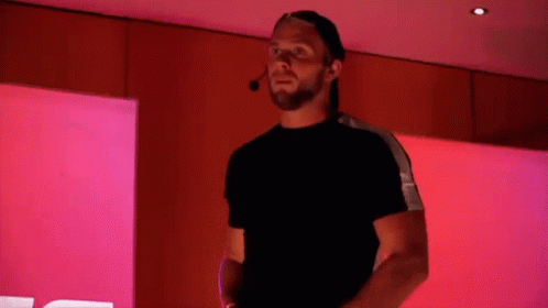 A Man With A Beard And A Hat Is Standing In Front Of A Pink Wall . GIF