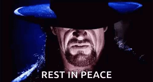 A Man With A Beard And A Hat Is Standing In The Dark . GIF