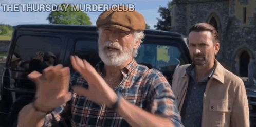 A Man With A Beard And A Hat Is Standing Next To Another Man In Front Of A Van . GIF
