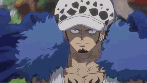 A Man With A Beard And A Hat Is Wearing A Blue Feathered Coat . GIF