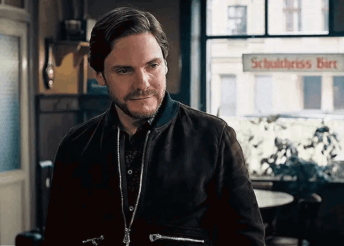 A Man With A Beard And A Jacket Is Standing In Front Of A Window In A Room . GIF