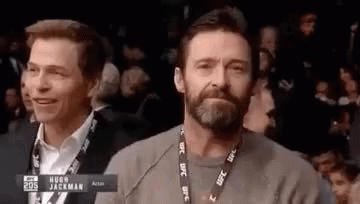 A Man With A Beard And A Lanyard Around His Neck Is Sitting In A Crowd Watching A Boxing Match . GIF