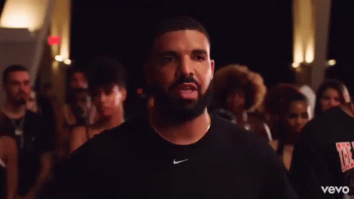 a man with a beard and a nike shirt is standing in front of a crowd of people .