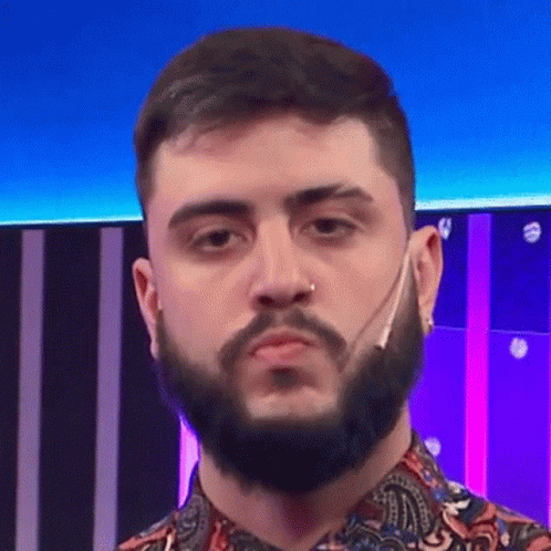 A Man With A Beard And A Nose Ring Is Wearing A Paisley Shirt And Making A Funny Face . GIF